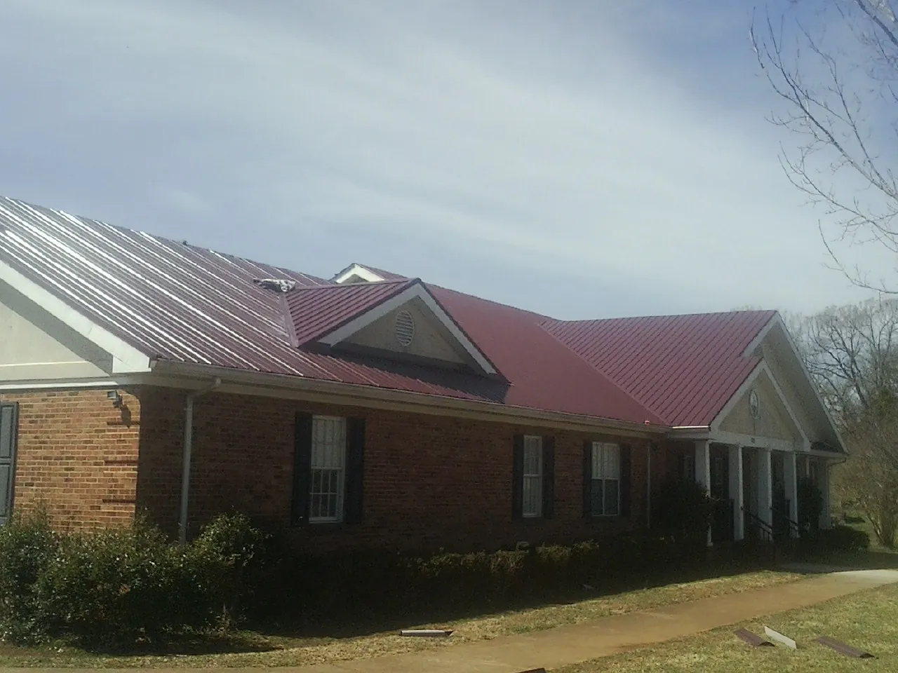 Red metal roof with gabled entries on a long brick building, from a Hail Damage Roof Repair job in San Clemente